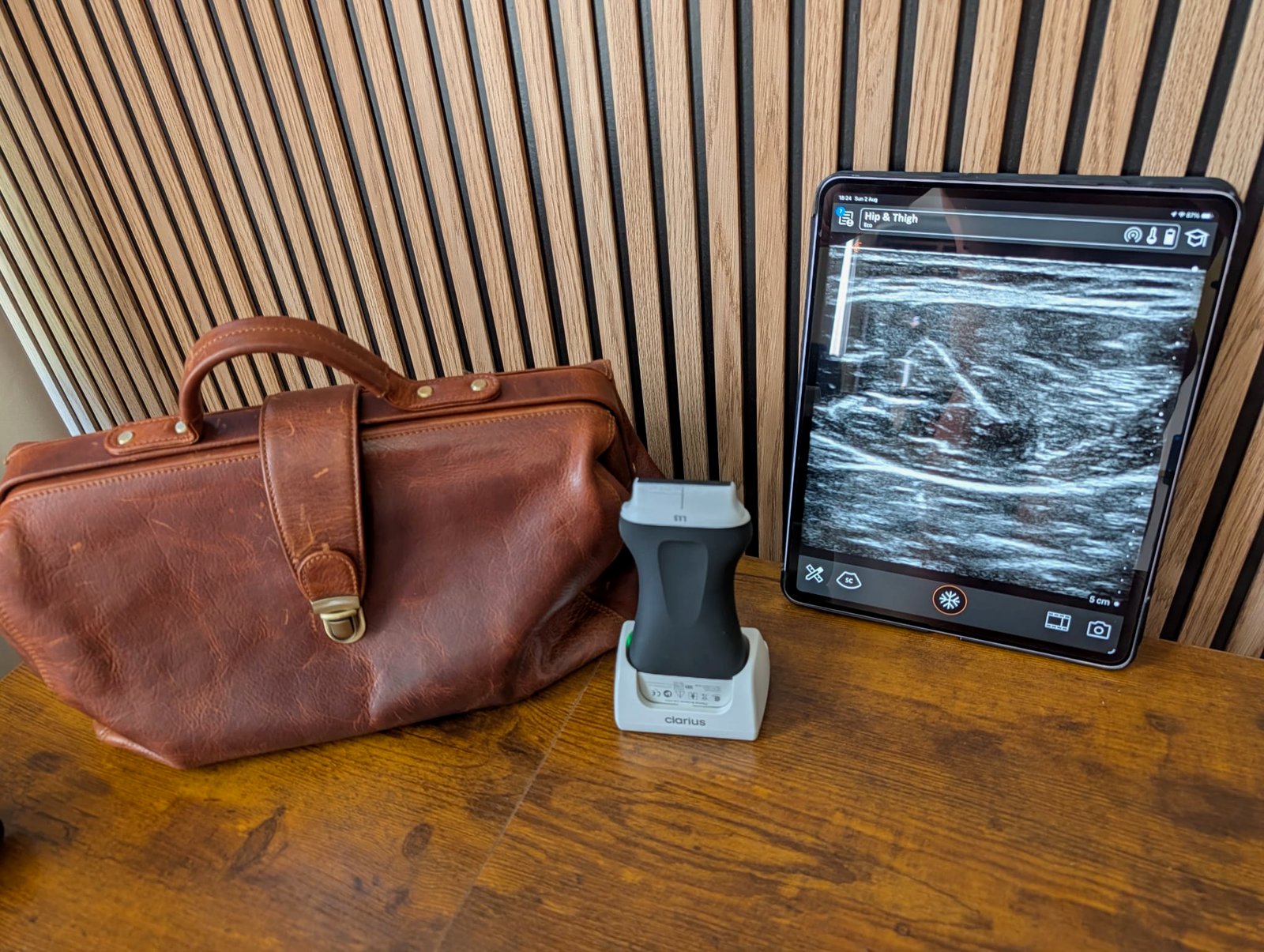 Ultrasound probe and tablet showing a quadriceps muscle scan beside a leather doctor bag