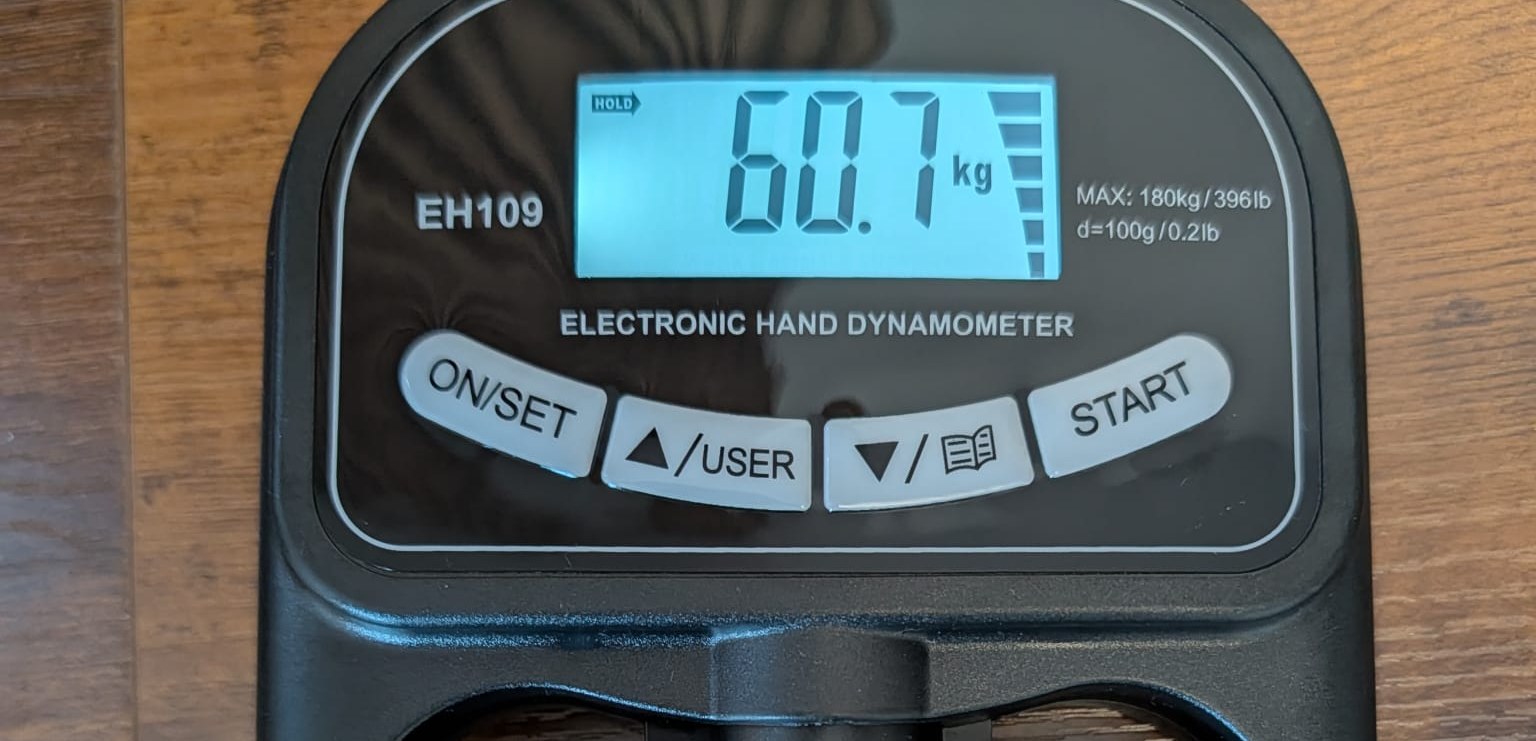 Electronic hand dynamometer on a table showing a grip strength reading in kilograms